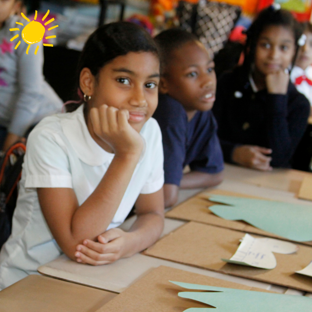 Three students sit at a desk with construction paper, ready to learn!
